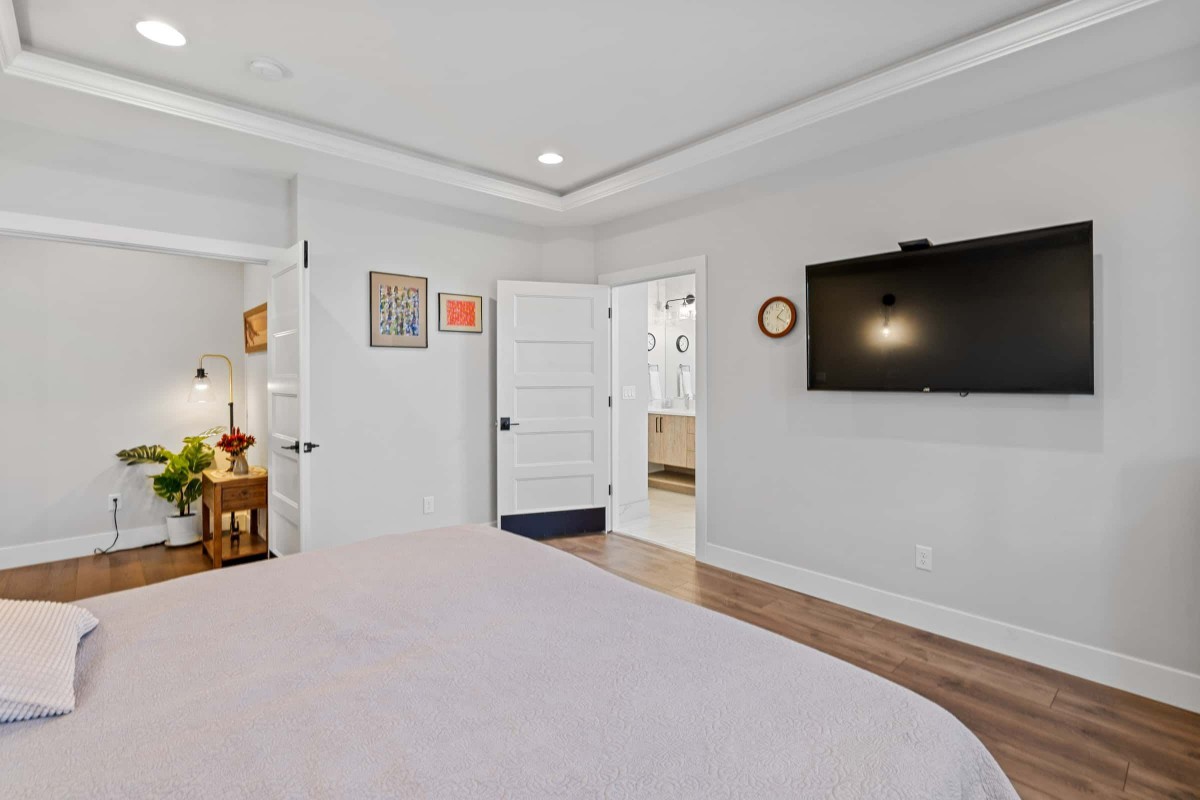 A modern bedroom with a wall-mounted TV, wooden flooring, and contemporary decor.