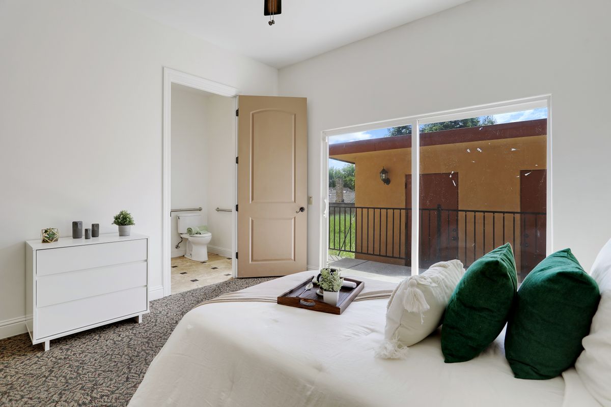 A minimalist bedroom with a neatly made bed, green accent pillows, and sliding glass doors leading to an outdoor view.