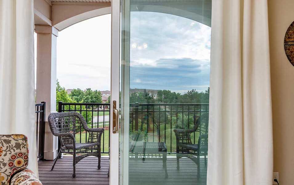 A cozy balcony with wicker chairs overlooks a scenic view through a sliding glass door.