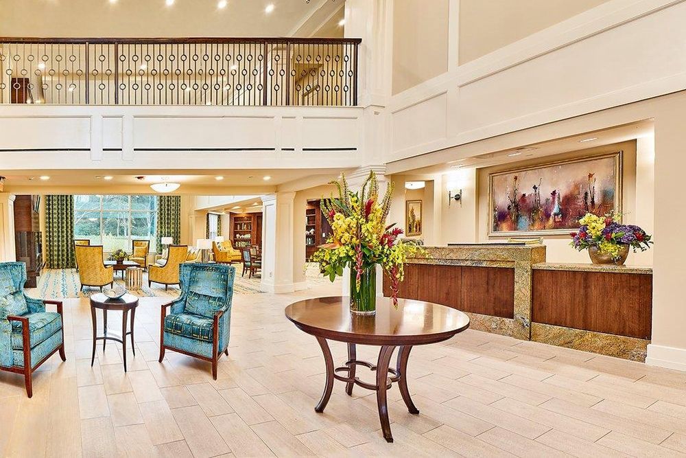 A spacious and elegantly decorated lobby with a central table, comfortable seating, and a reception desk.