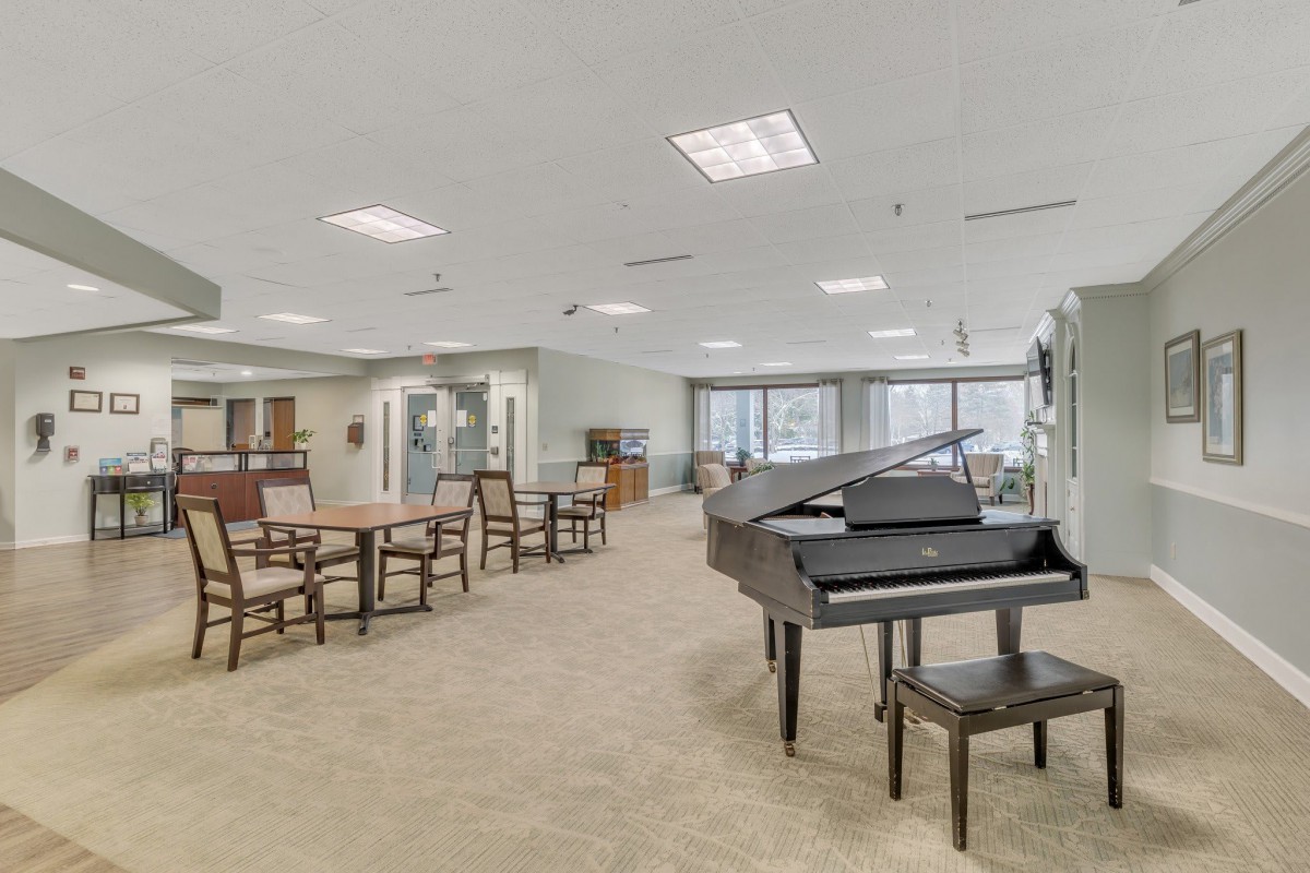 A spacious and well-lit lounge area featuring a grand piano, tables, and chairs.