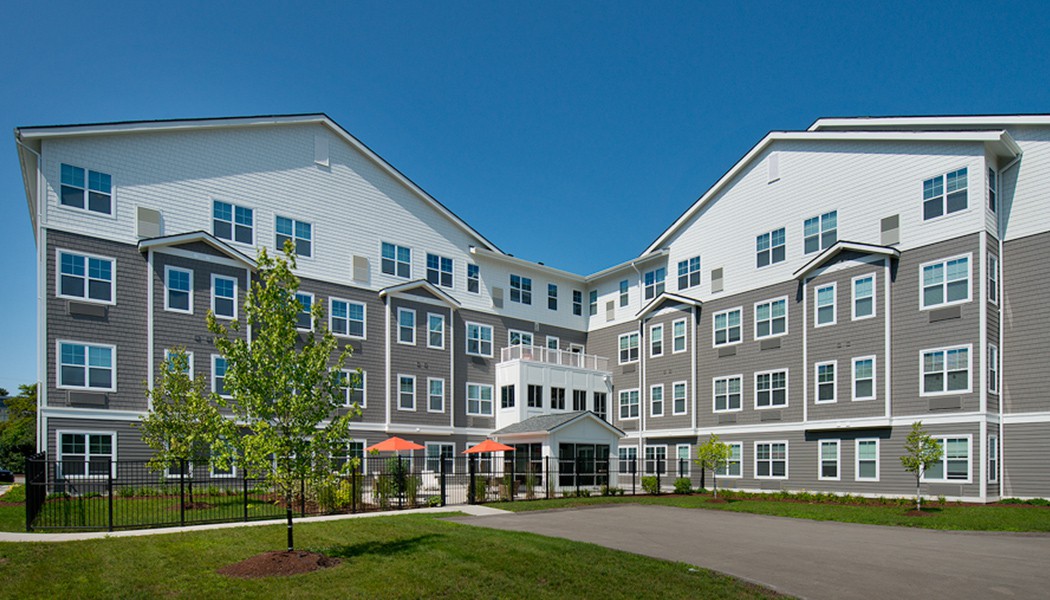 A modern multi-story residential apartment building with well-maintained landscaping under a clear blue sky.