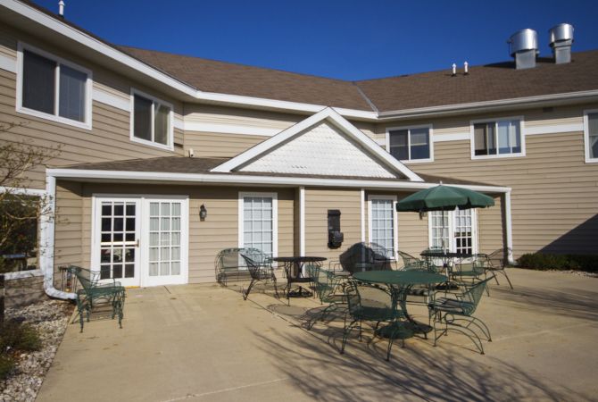 A sunny patio area with tables and chairs in front of a two-story building.