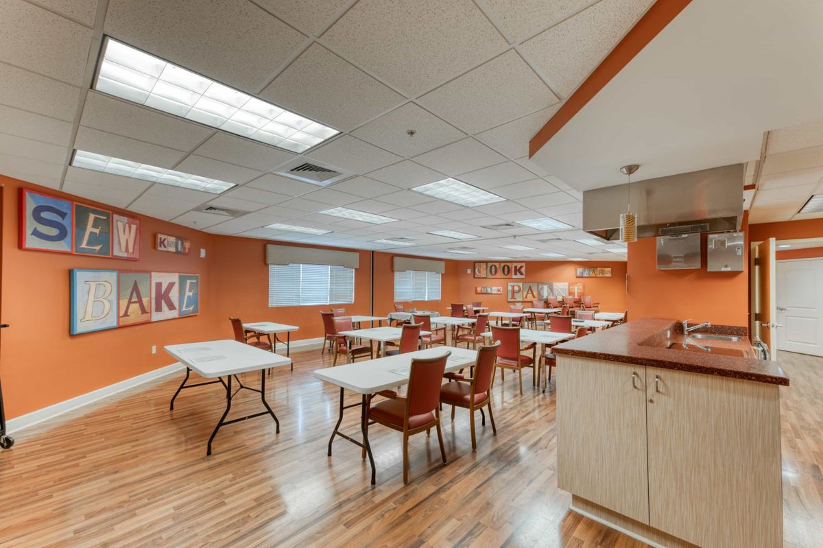 A modern classroom with orange walls, arranged tables and chairs, and ample natural light.