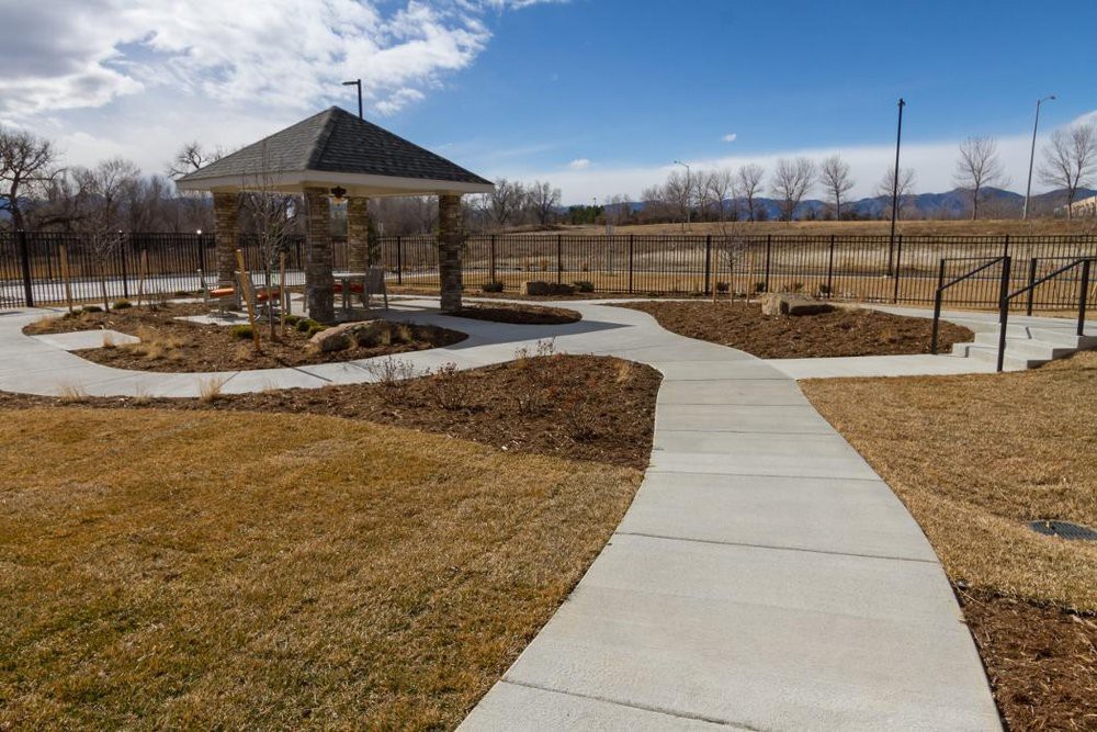 A well-maintained park with a concrete pathway leading to a pavilion under a clear blue sky.