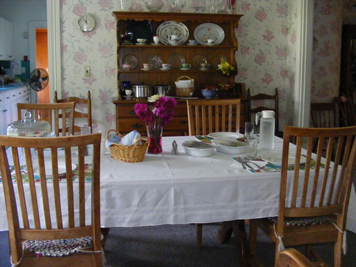 A cozy dining room with a table set for a meal, featuring a vase of flowers and a china cabinet in the background.