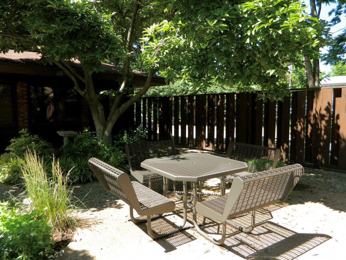 A tranquil patio with garden furniture shaded by trees.