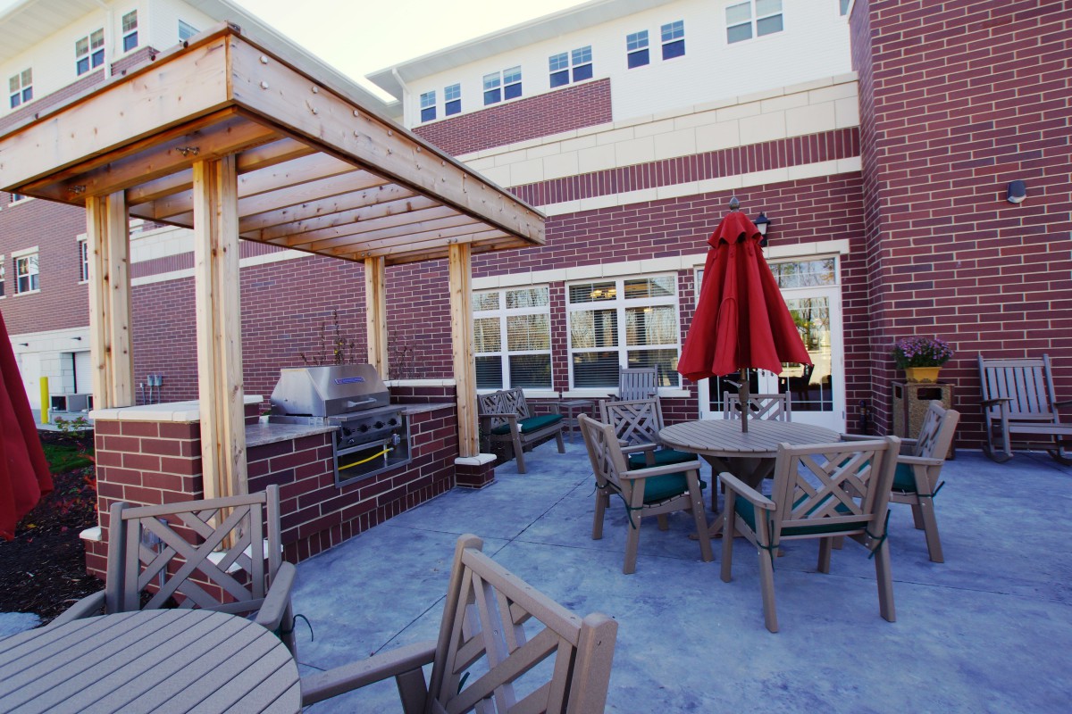An outdoor patio area with tables, chairs, and a red umbrella next to a brick building.