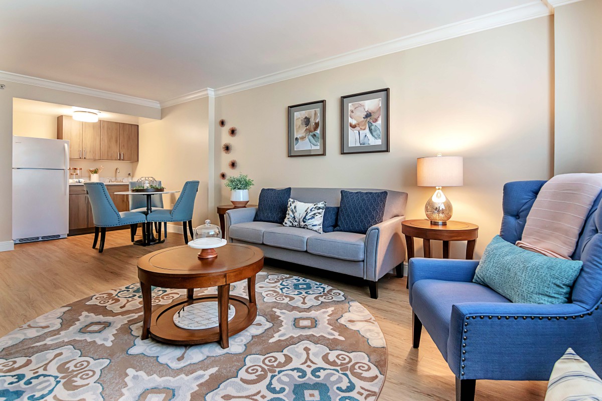 A cozy living room with a gray sofa, blue armchairs, and a round wooden coffee table, complemented by a dining area in the background.