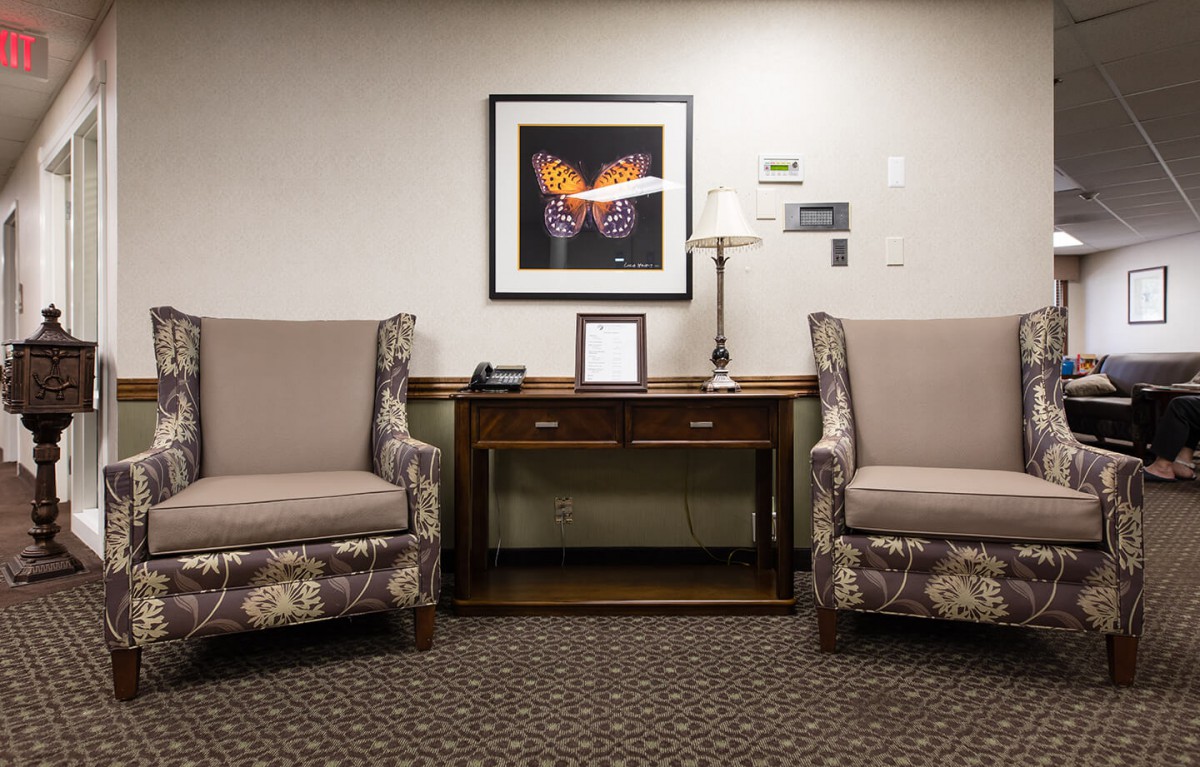 A waiting room with two upholstered chairs, a wooden table, and butterfly artwork on the wall.