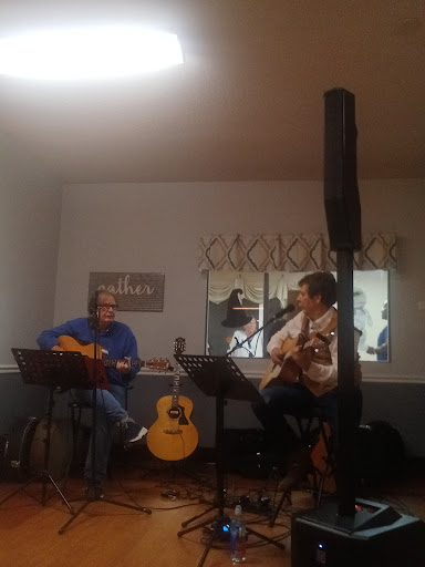 Two musicians performing together with acoustic guitars in a cozy indoor setting.