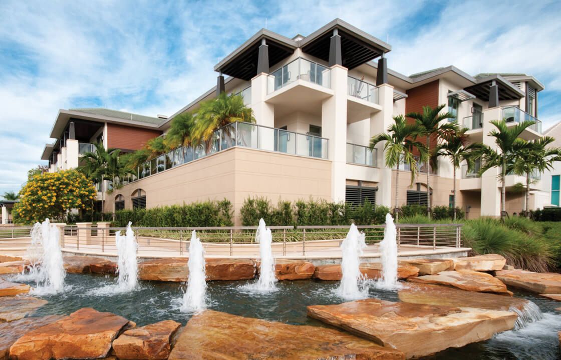 A modern building with fountains and palm trees in the foreground.