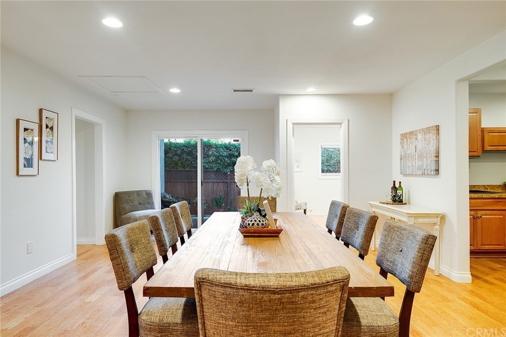 A modern dining room with a large wooden table and upholstered chairs, featuring minimalist decor and bright lighting.