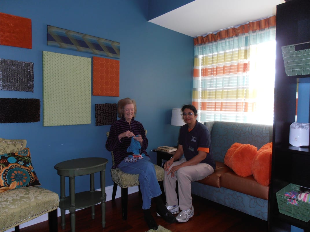 Two people sitting in a brightly decorated living room with blue walls and vibrant cushions.