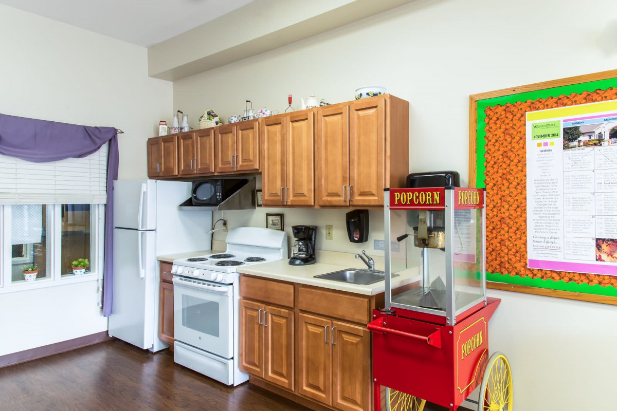 A kitchen with wooden cabinets, a stove, refrigerator, microwave, and a popcorn machine on the counter.