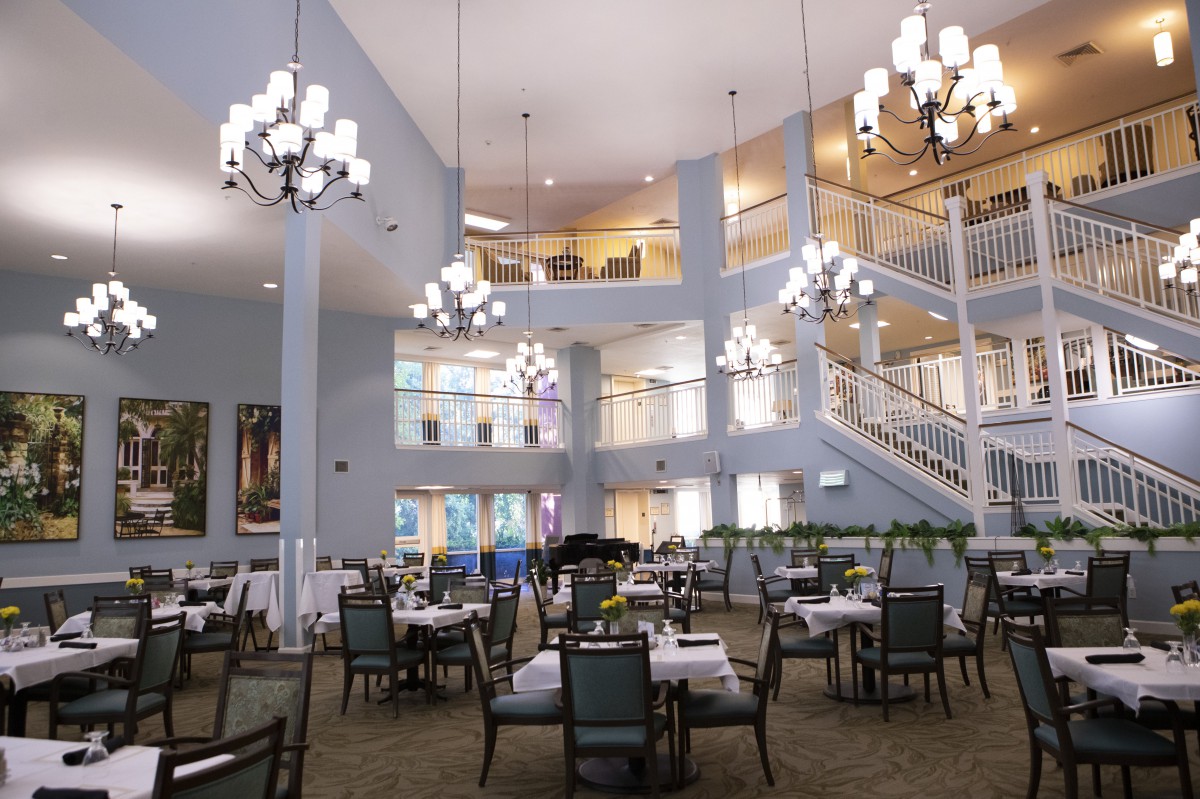 A spacious and elegant dining area with multiple levels, featuring rows of tables and chairs under beautiful chandeliers.