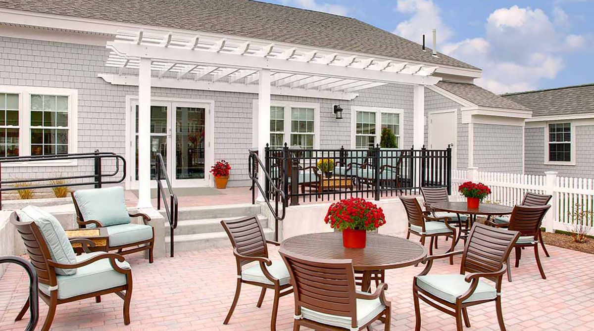 A well-furnished outdoor patio with a pergola, featuring tables and chairs, decorated with flower pots.