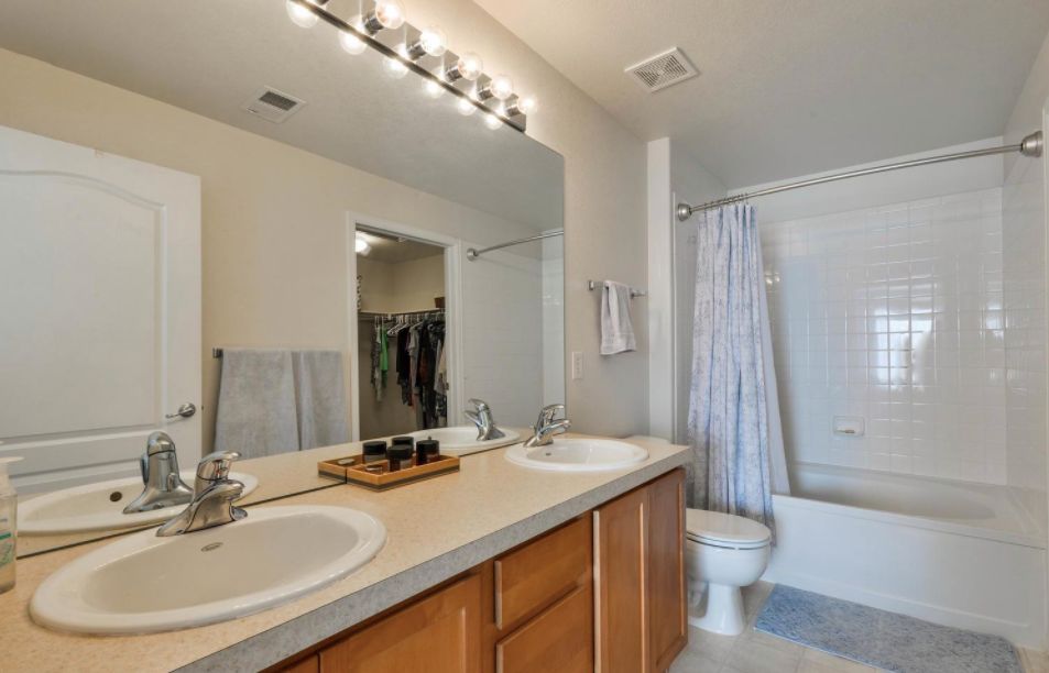 A modern bathroom featuring a double sink vanity and large mirror, with a shower area enclosed by a curtain.