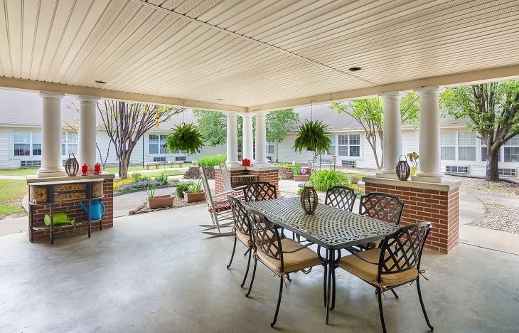 A spacious covered patio with a dining table and chairs, surrounded by a garden and potted plants.