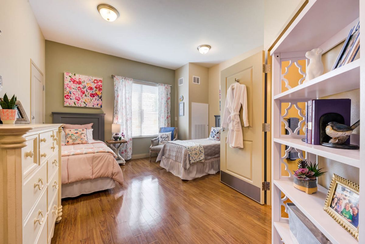 A cozy bedroom with two beds and bright natural light, featuring hardwood floors and decorative art.