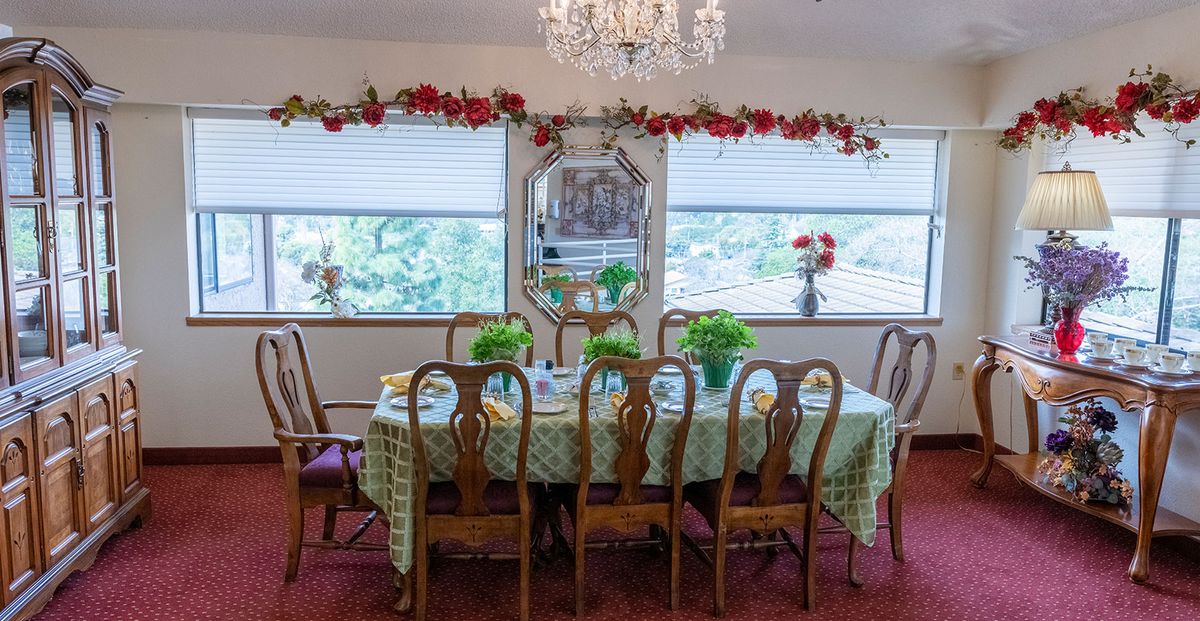 A well-decorated dining room with a long table set for guests, featuring a chandelier and greenery accents.