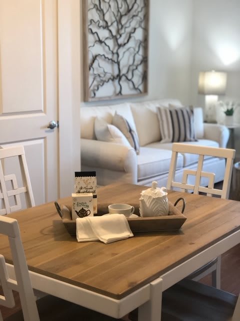 A cozy living room with a wooden dining table adorned with a decorative tray set, complemented by neutral-colored furniture and soft lighting.