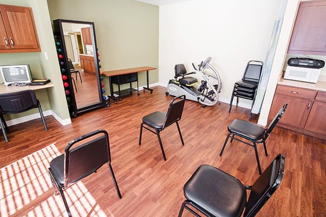 A small exercise room with chairs arranged in a circle and a stationary bike in the corner.