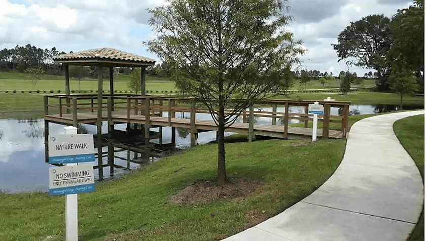 A scenic view of a park with a wooden bridge over a pond, surrounded by lush greenery.