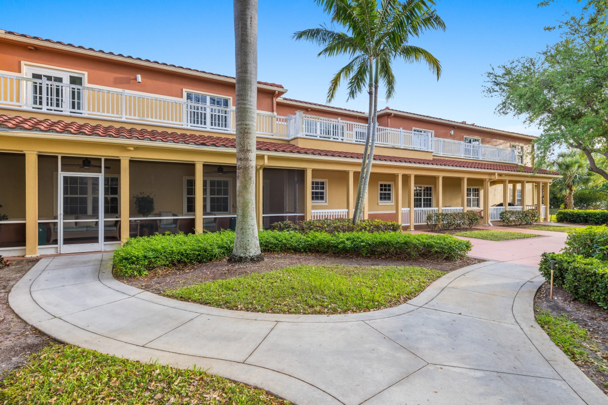 A two-story building with a landscaped walkway and palm trees in front.