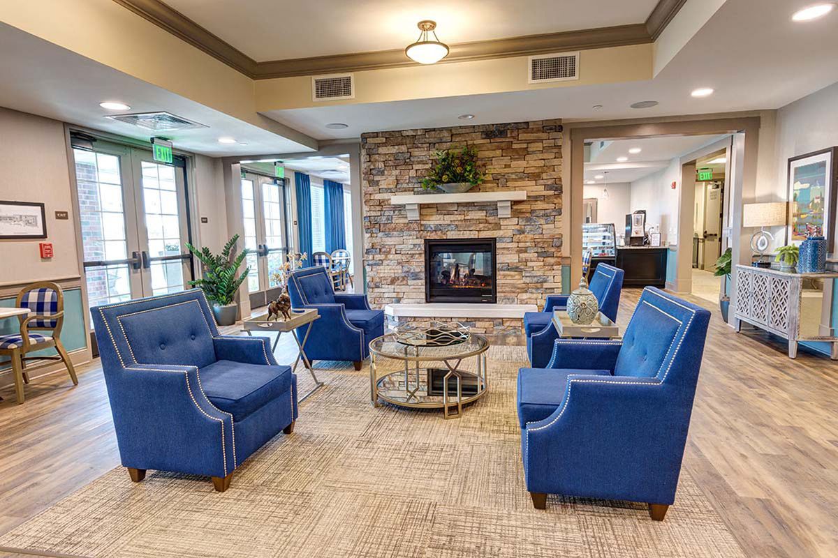 A modern living room with blue armchairs arranged around a glass coffee table, centered by a stone fireplace.