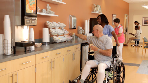 A caregiver assists an elderly individual in a wheelchair at a snack station.