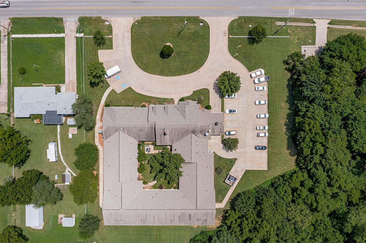 An aerial view of a building with an adjacent parking lot, surrounded by trees and grass.