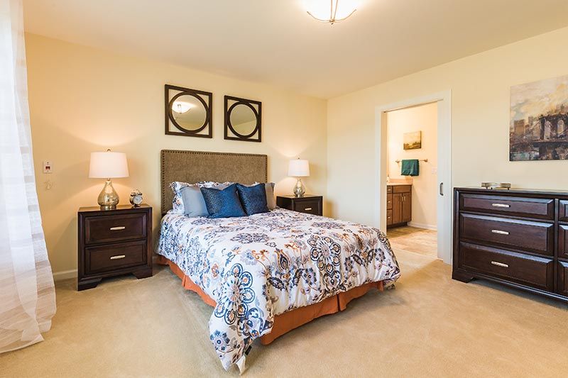 A cozy bedroom with elegant decor featuring a bed, two lamps, and decorative mirrors on the wall.