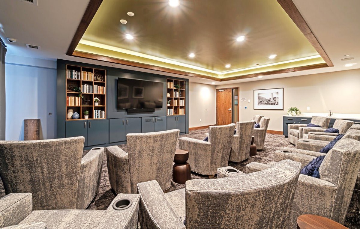 A cozy home theater room with comfortable seating and a large screen, surrounded by bookshelves and warm lighting.