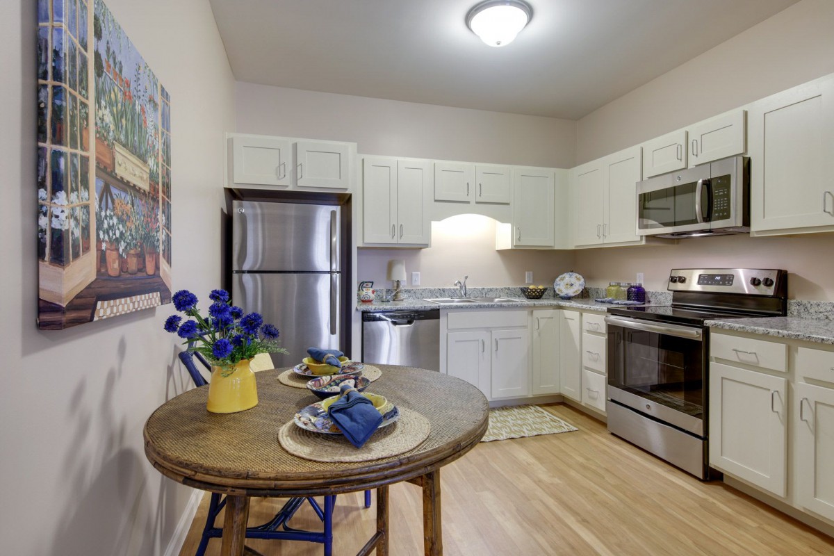 A modern kitchen with a small dining area featuring stainless steel appliances and white cabinetry.