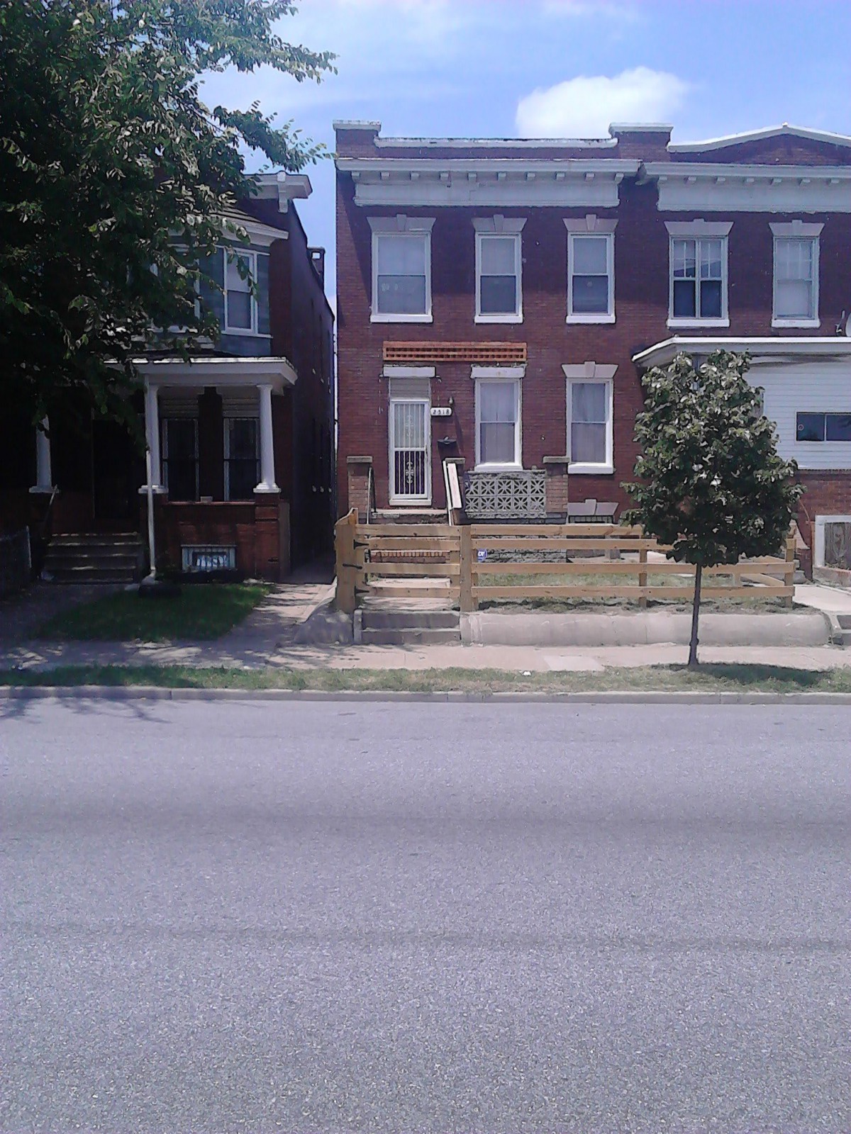 A street view of a brick residential house with a small front yard and a tree.