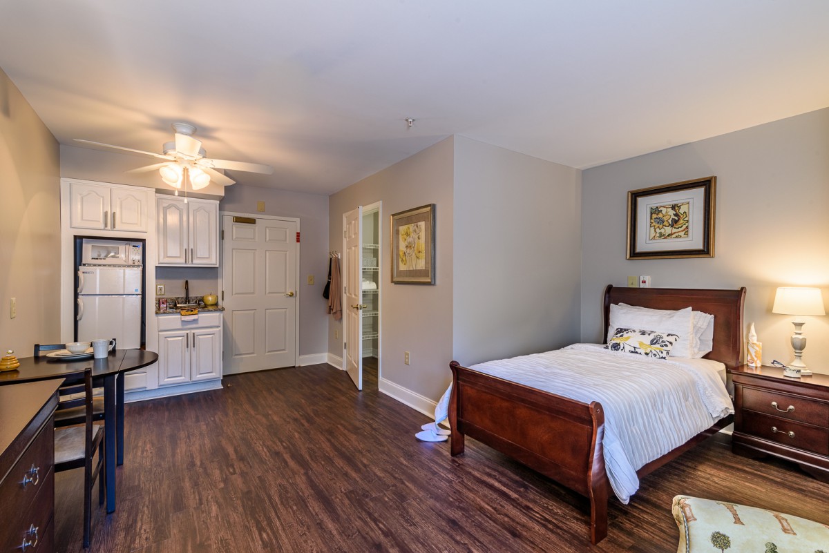 A cozy bedroom with wooden flooring, featuring a single bed and a kitchenette.