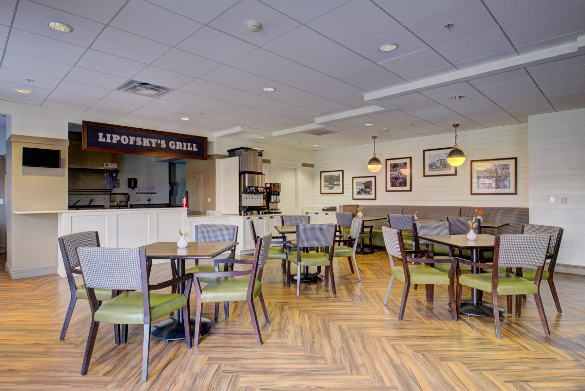 An empty cafe interior with wooden floors, tables, and chairs, featuring framed art on the walls.