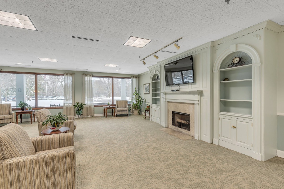 A cozy living room with a fireplace and television, featuring comfortable seating and large windows.