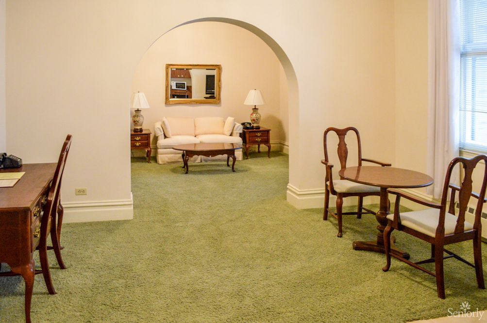 A cozy living room with elegant furniture and a green carpet, featuring a sofa, lamps, and archway.