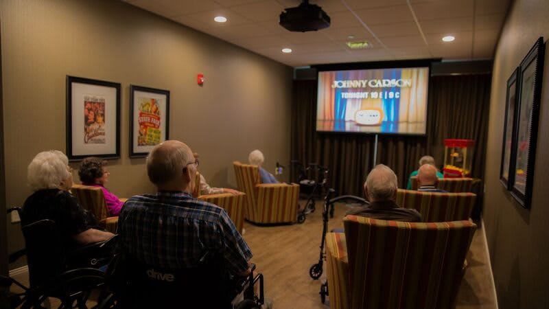 Elderly residents watching a movie in a care home's cinema room.