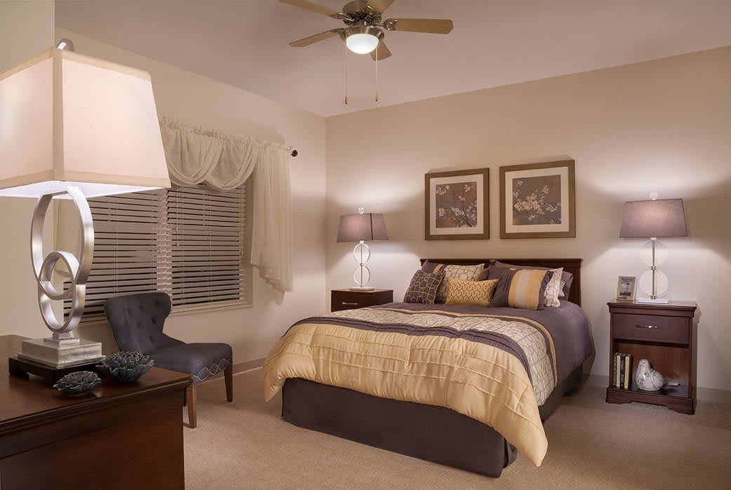 A cozy and well-decorated bedroom with neutral tones, featuring a comfortable bed, stylish lamps, framed artwork, and a plush chair.
