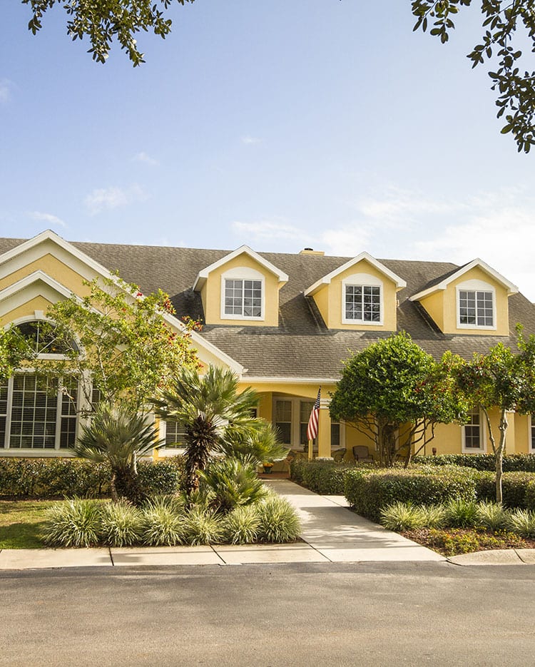 A yellow suburban house with lush landscaping and a sunny day.