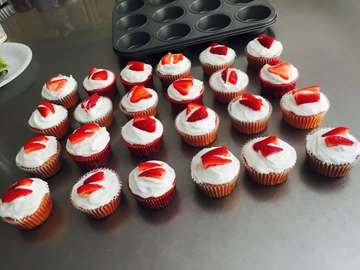 A batch of freshly baked cupcakes topped with strawberry slices and frosting.
