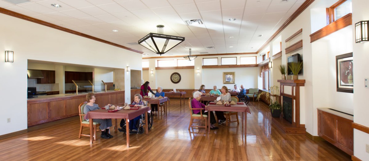 A communal dining area in a senior living facility with people seated at tables.