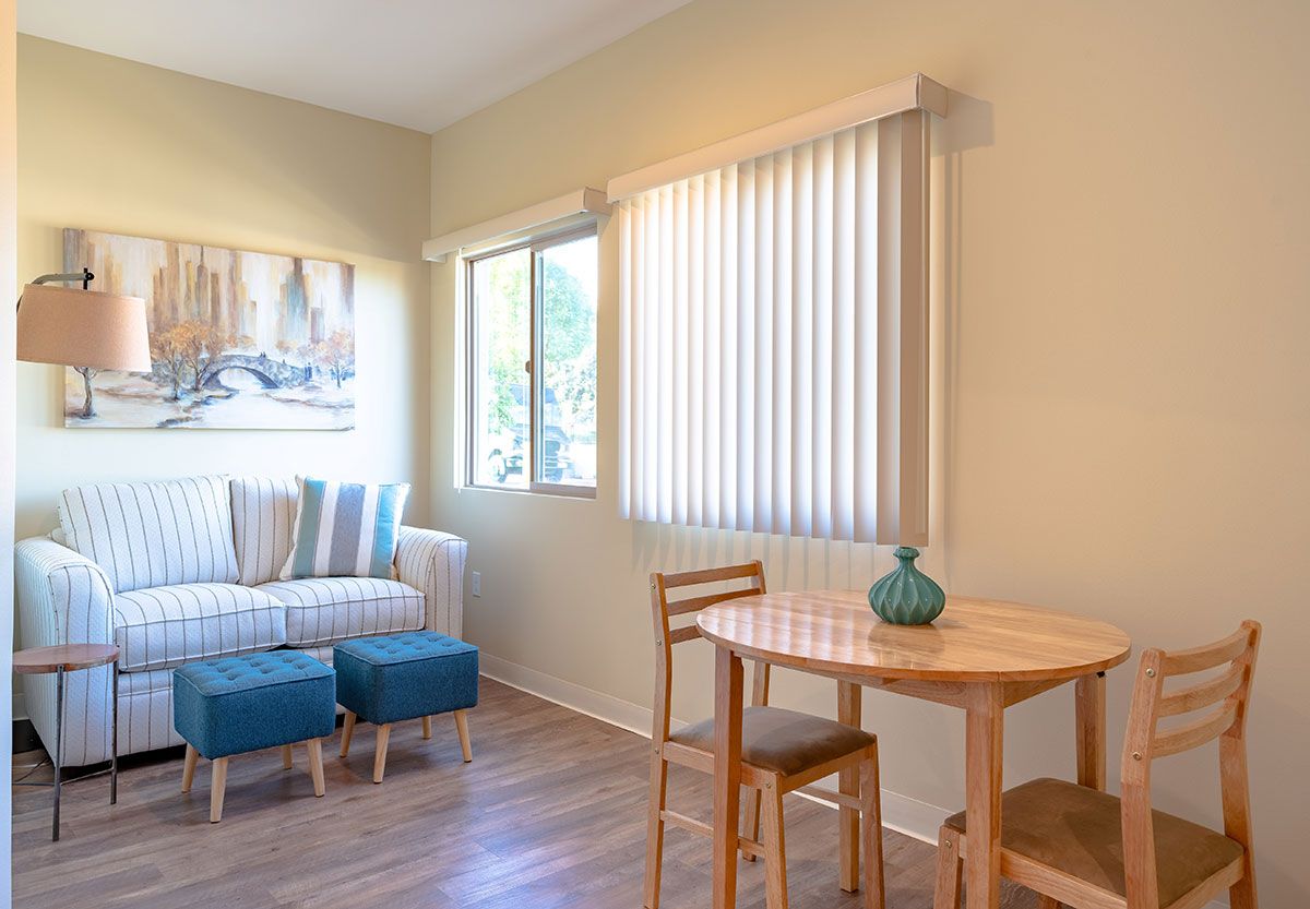 A cozy living room with a small table and chairs by the window, featuring a striped sofa and blinds.
