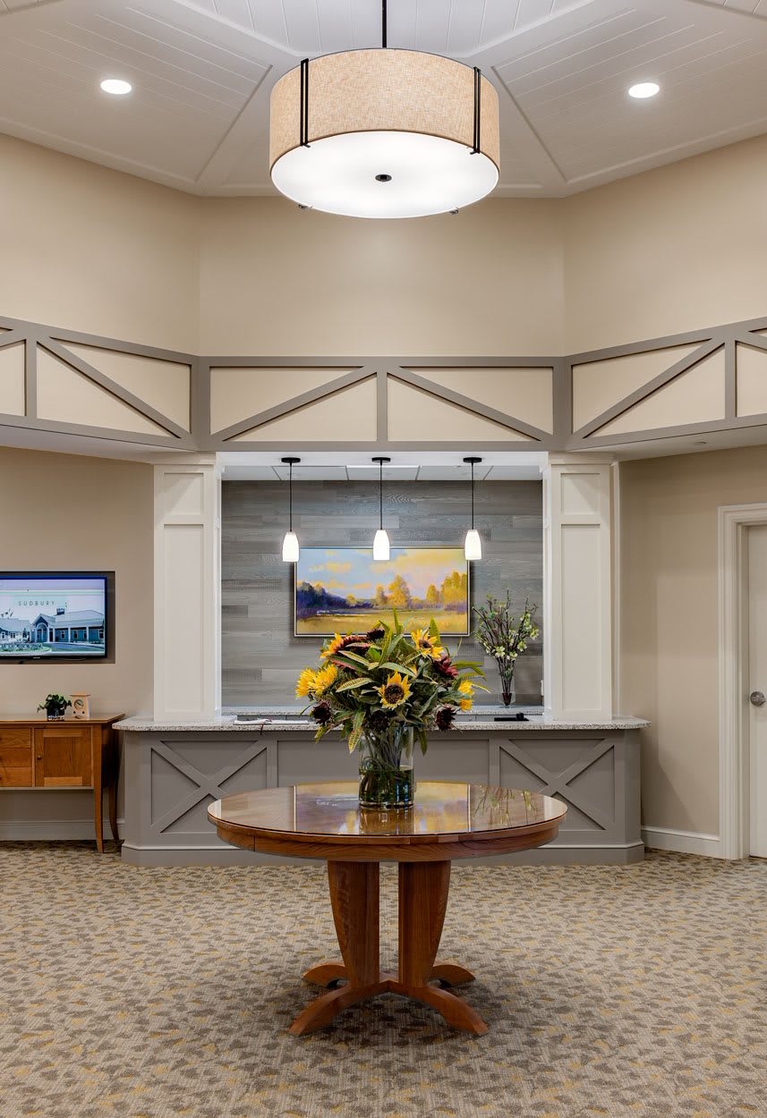 A welcoming reception area featuring a round table with a floral arrangement, artwork on the walls, and modern lighting.
