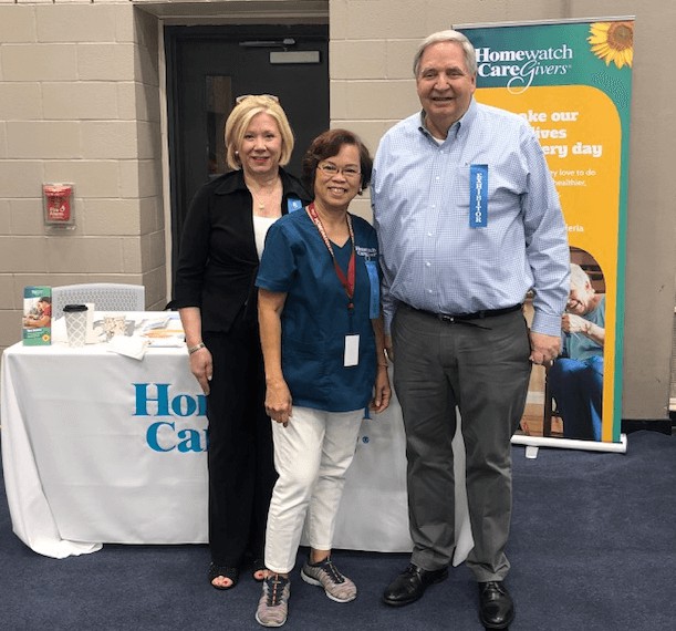 A group of three individuals standing in front of a healthcare exhibition booth at a conference event.