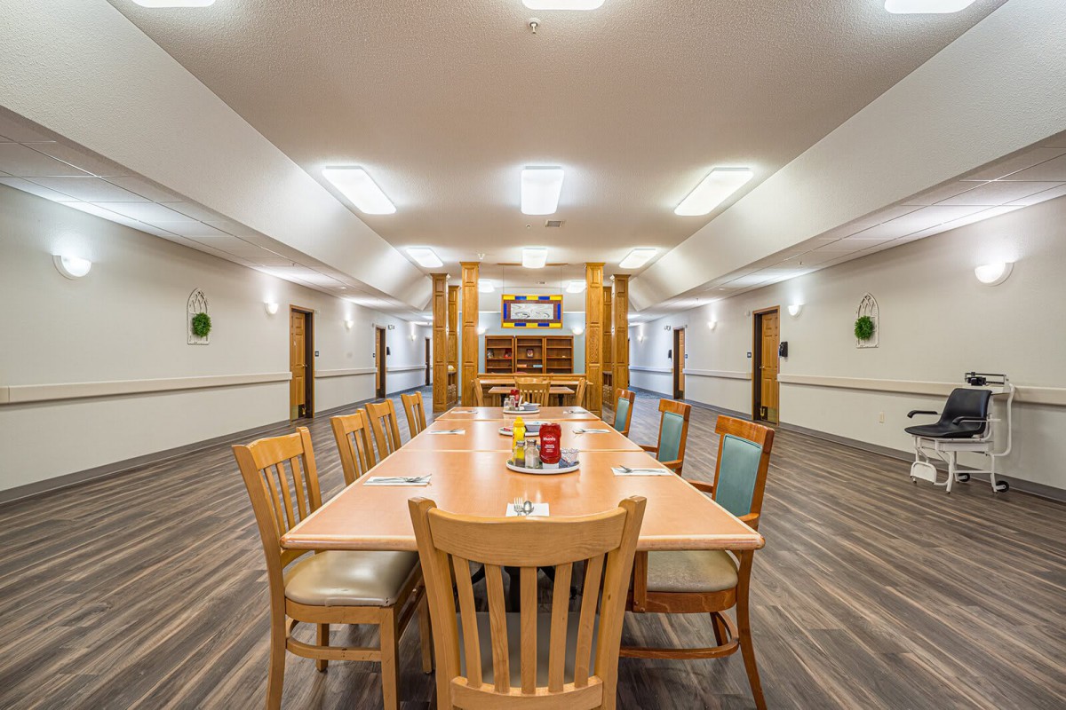 A well-lit dining or meeting room with a long wooden table and chairs.