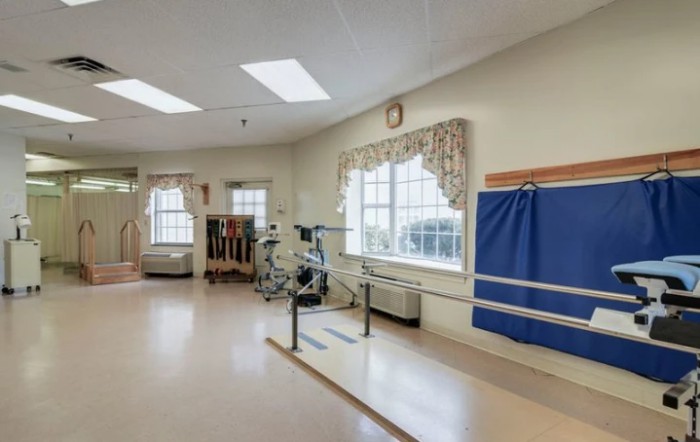 A rehabilitation room equipped with parallel bars and exercise equipment under bright lighting.